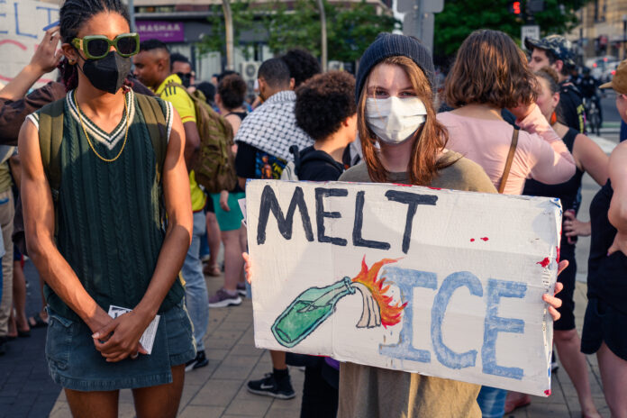 Two protestors are present at a protest against ICE in Washington DC, one is holding a poster that says "Melt ICE" on June 10, 2025.