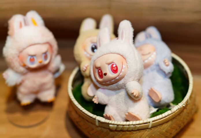 Three Labubu toys are piled into a woven basket while one labubu sits outside of the basket.