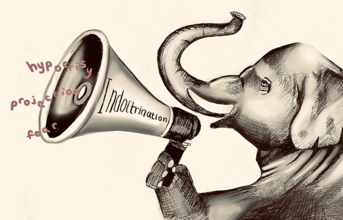 An elephant is holding a megaphone with “Indoctrination” written on it while words like “hypocrisy, projection, and fear” are coming out of the megaphone.