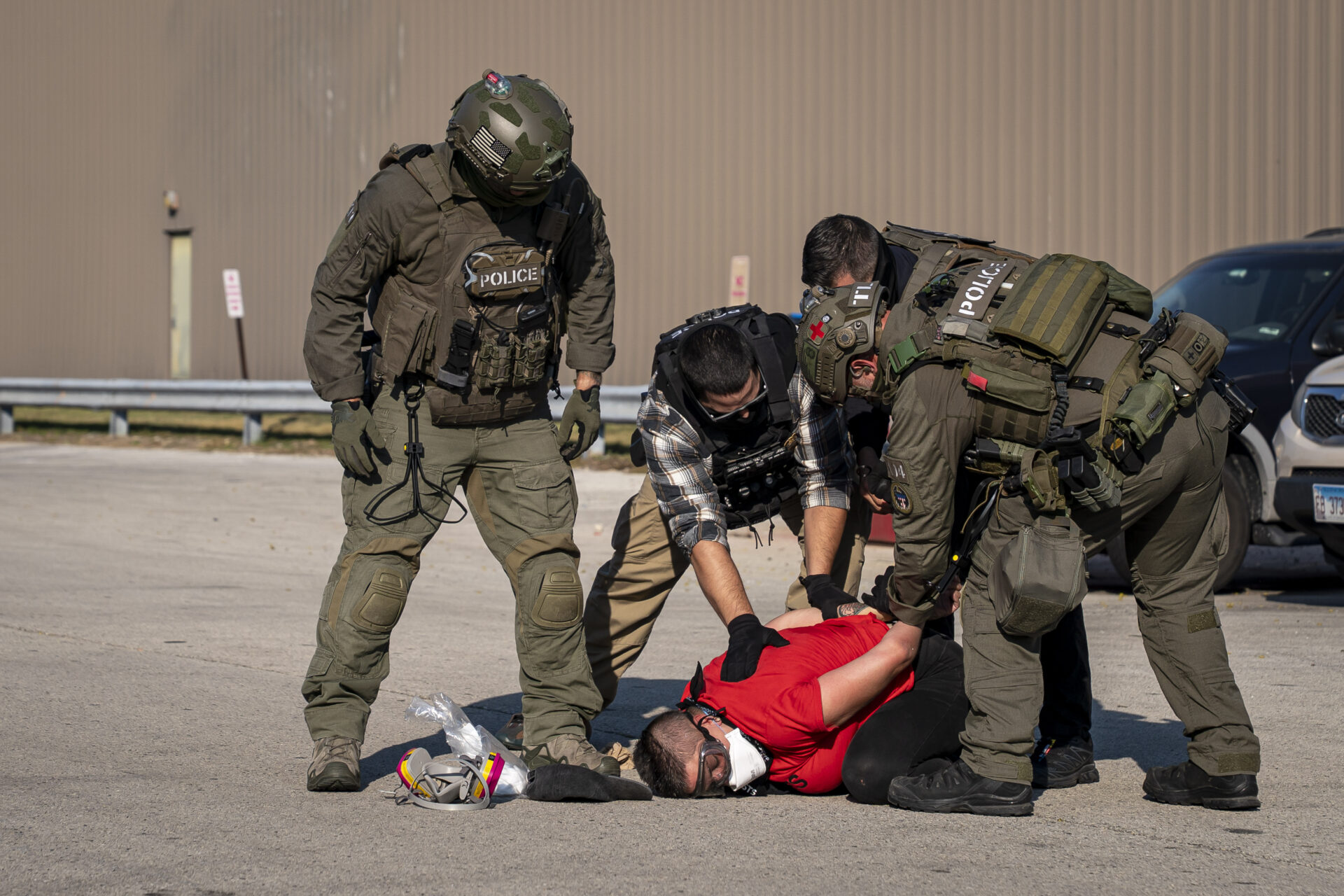 Four Immigration Control Enforcement agents are shown putting a man in a red shirt in hand cuffs on the floor.